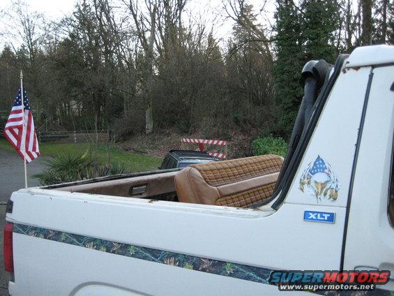 White 1980 Ford Bronco XLT with brown quilted seats and camouflage trim, viewed from the rear