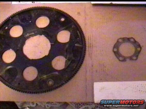 Large black flexplate with circular cutouts and a smaller metal spacer ring on a wooden surface