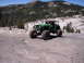 1989 Ford Bronco - A heavily modified green jeep navigates a rocky, off-road trail in a mountainous landscape.