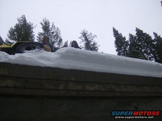 Yellow vehicle partially buried in snow with two people visible