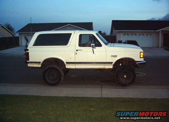 White lifted Ford Bronco, side view, showing modified suspension and large tires