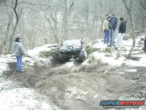 Jeep Wrangler navigating a muddy, snowy trail with onlookers