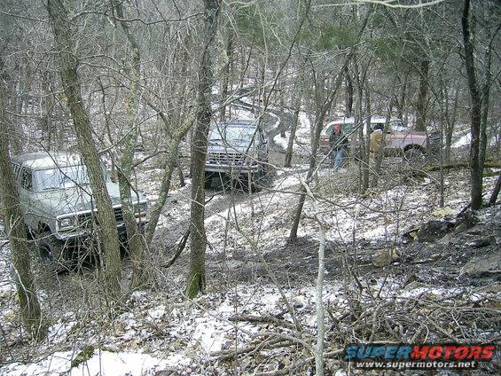 1978 Ford Bronco driving on a muddy trail through trees