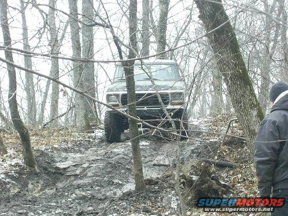 Dark 1978 Ford Bronco climbing a muddy hill in a wooded area