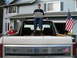 1980 Ford Bronco - A person sits on the tailgate of a Ford pickup truck with a laptop, an American flag flies from the fender.