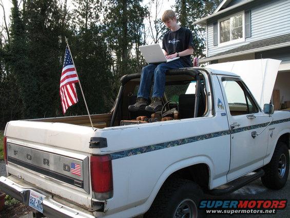 White 1980 Ford Bronco rear view with American flag and person on laptop