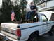 1980 Ford Bronco - A white 1980 Ford Bronco is seen from the rear, with an American flag flying and a person using a laptop on top.