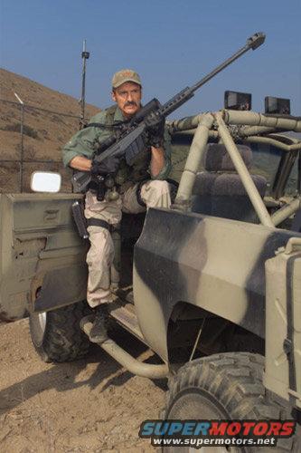 Man in camouflage uniform holding a sniper rifle, sitting in a military-style vehicle with camouflage paint