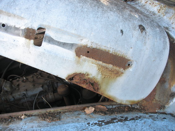 Close-up of a rusted white fender over a dark engine compartment