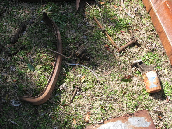 Rusted metal parts including a curved piece, a spring, and a cylindrical object scattered on grass