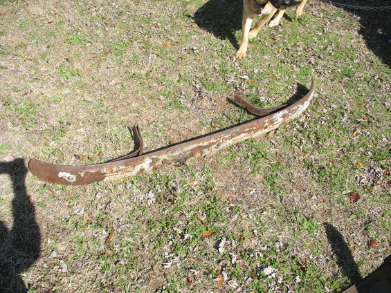 Rusted bumper with curved ends and mounting brackets on grassy ground