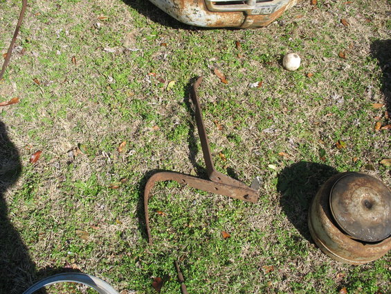 Rusty metal tool with a curved end and a round metal part on grass