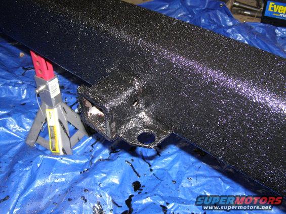 Black rear bumper section with a tow hitch receiver and wiring harness