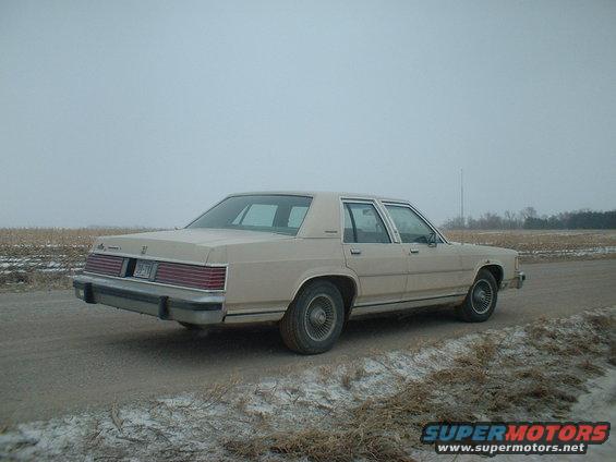 1987 Mercury Grand Marquis sedan, rear view, parked on dirt road with fields in background