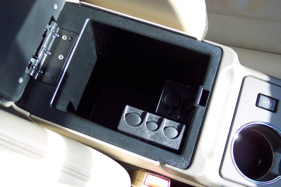 Car's open center console storage with a power outlet and coin holder