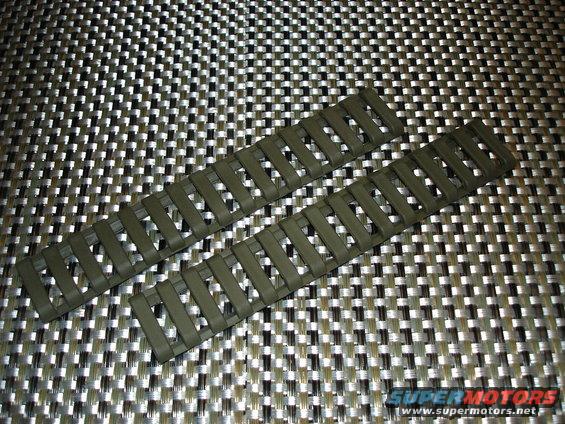Two olive drab rail covers on a textured surface. The covers have a slotted design
