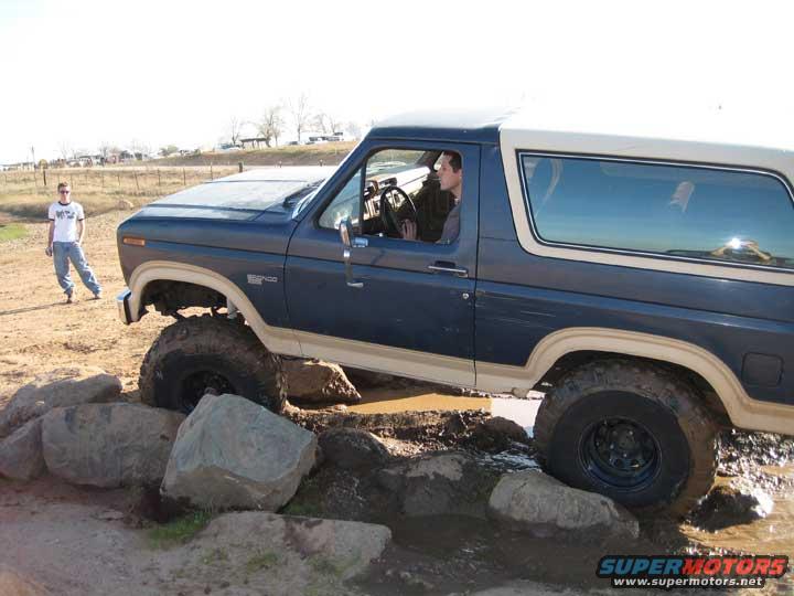 Blue and tan 1978 Ford Bronco navigating rocks and mud
