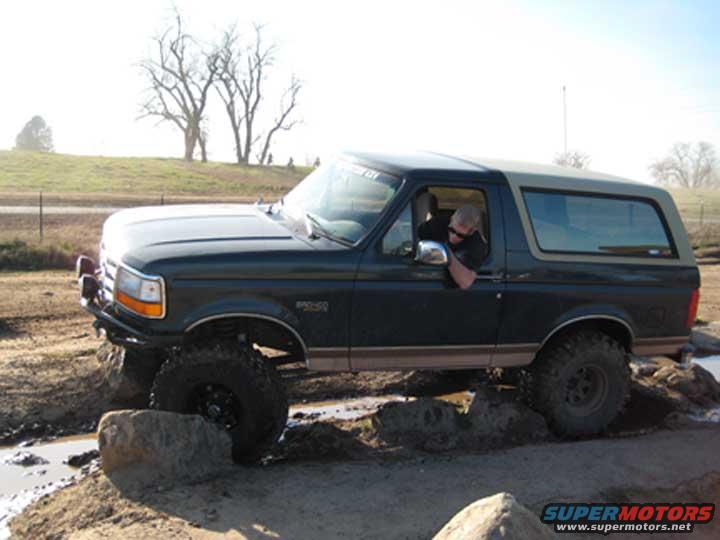 Dark green Ford Bronco with a tan top, driving over rocks and mud