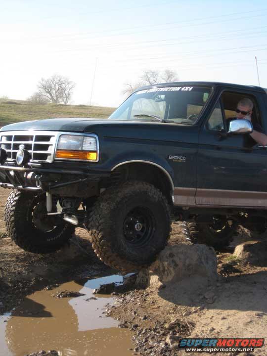 Dark green Ford Bronco with lifted suspension navigating muddy terrain