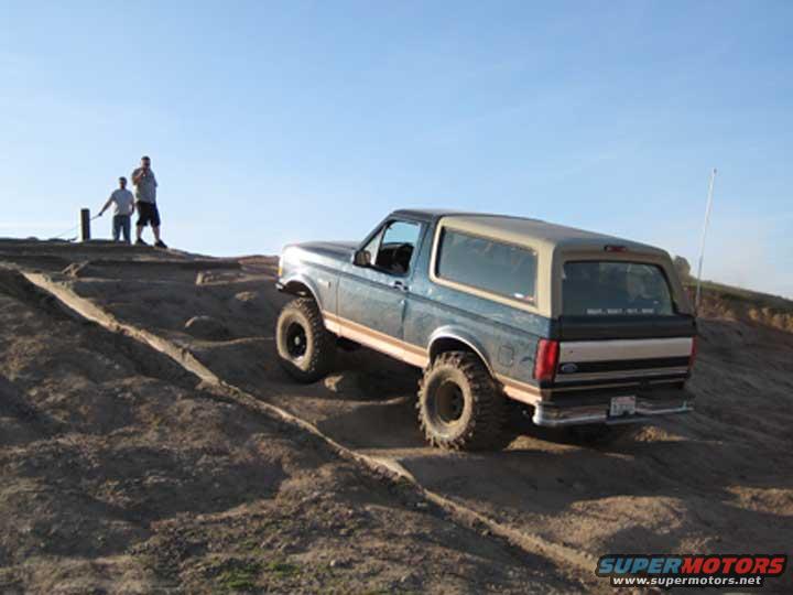 Blue and tan SUV with large tires driving on a dirt hill