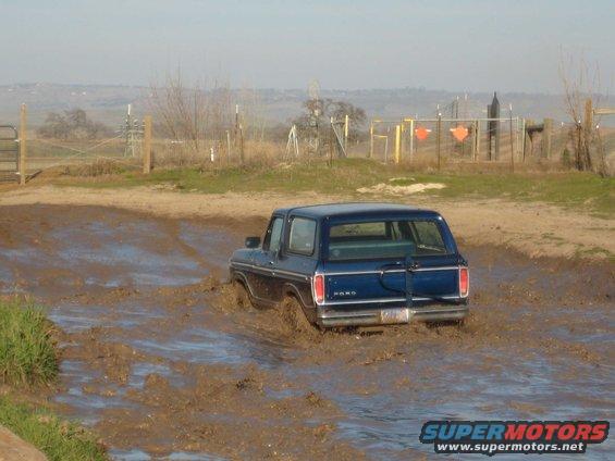 Blue 1978 Ford Bronco driving through a muddy field
