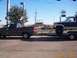 2004 Ford F-150 - A brown pickup truck tows a lifted Ford F-250 Super Duty on a trailer down a road.