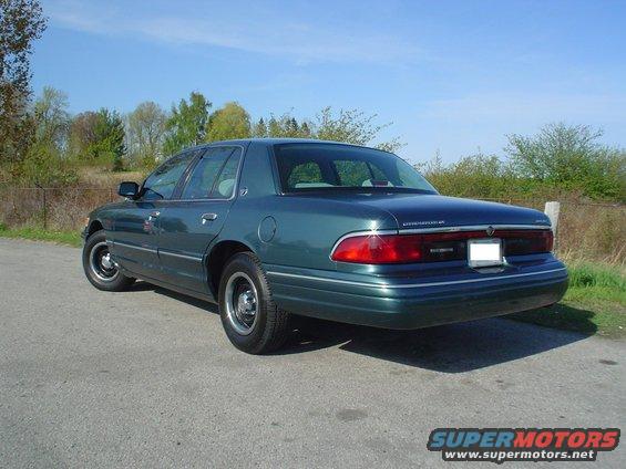 Green sedan parked on asphalt, rear-right quarter view. Chrome trim along the bottom body line. Clear sky above