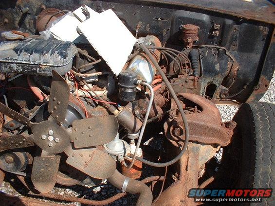 Engine bay of a rusty car with a fan, radiator, and engine parts visible