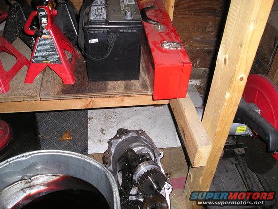 Transfer case with gears and chain, next to a car battery, toolbox, and jack stands