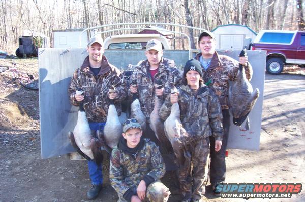 Group of hunters with geese in front of a truck bed, with a red Ford Bronco in the background