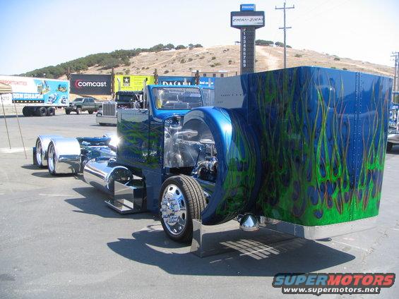 Blue semi-truck with green flame graphics, chrome fenders, and exposed engine