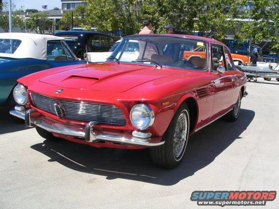 Red coupe with chrome grille and hood scoop parked outdoors