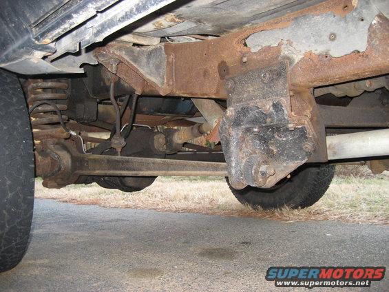 Underside of a vehicle showing rusty frame, suspension components, and tires