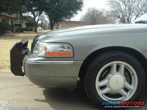 Front corner of a silver 2003 Mercury Grand Marquis with a black push bar and a basketball hoop in the background