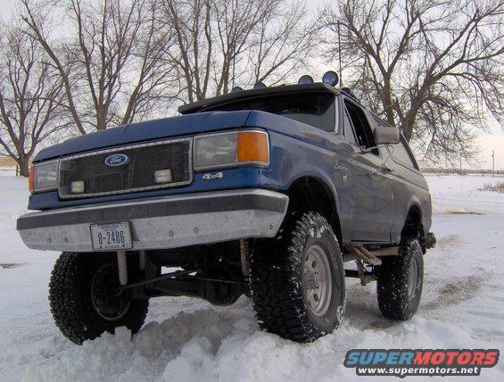 1987 Ford Bronco with lifted suspension and off-road tires in snow. License plate reads 8-2486