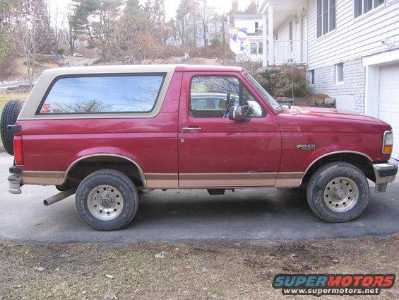 Red Ford Bronco with tan removable top, spare tire on back. Side view