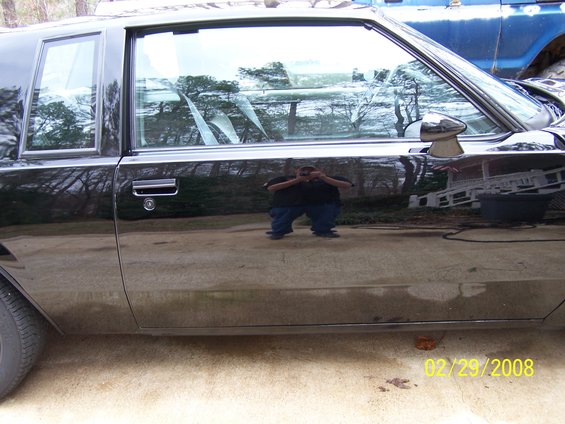 Black car side view, reflection shows a person crouching. Date stamp reads 02/29/2008