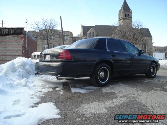 Black 2000 Ford Crown Victoria parked on asphalt with snow piles. Rear view shows taillights and exhaust pipe