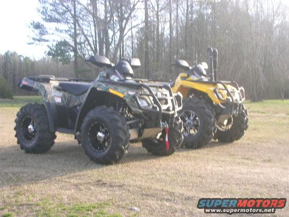 Two all-terrain vehicles parked on grass, one camouflage and one yellow, with trees in the background