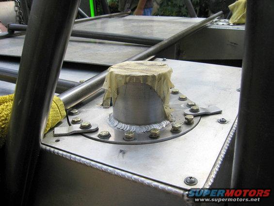 Fuel tank filler neck with tape covering it, bolted to a metal surface. Supermotors.net logo visible