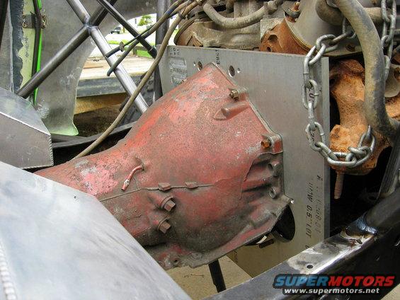 Red transmission housing bolted to engine block with metal plate and chain