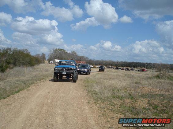 Blue pickup truck driving on a dirt road with other vehicles behind it