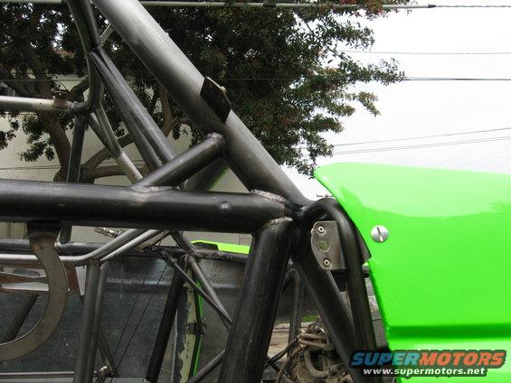 Close-up of a custom roll cage with green body paneling. A Supermotors logo is visible at the bottom right