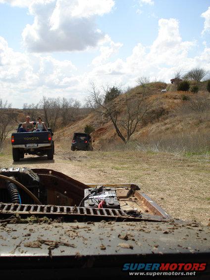 Toyota pickup with people in bed driving on dirt road, another SUV behind it