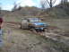 2008 International School Bus - A blue pickup truck is stuck in a muddy ditch, with its doors open.