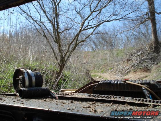 Truck radiator and a tire on a muddy surface, with trees and a dirt path in the background