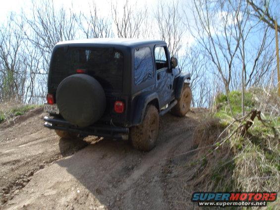 Black Jeep Wrangler with spare tire on rear, driving up a dirt hill