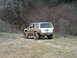 2008 International School Bus - A white Jeep Cherokee, modified for off-roading, navigates a muddy trail through a wooded area.