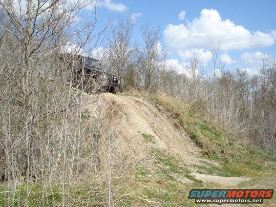 Dark SUV climbing a dirt hill through dry brush