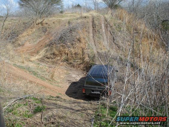 Jeep Cherokee XJ driving up a muddy, rutted dirt trail through dry brush